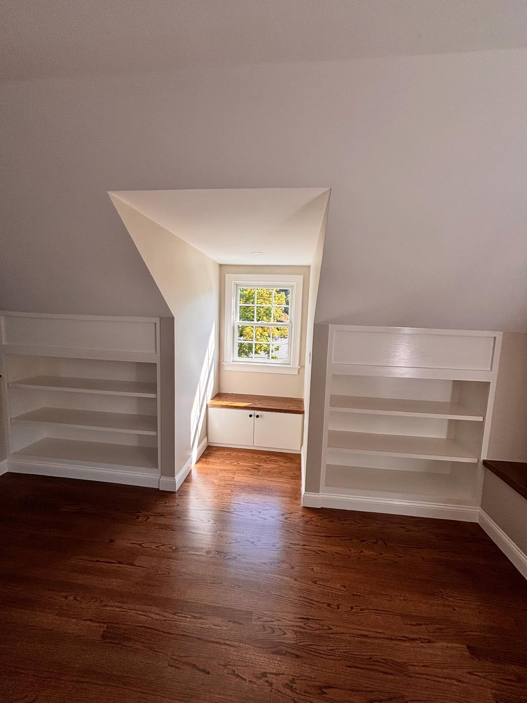 Finished attic room with custom white built-ins and red oak flooring